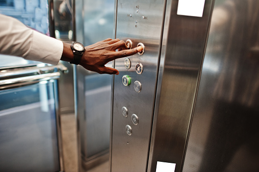 Foto de mano de hombre del afroamericano con relojes en elavator o moderno ascensor, pulsando botón de cerca. photo