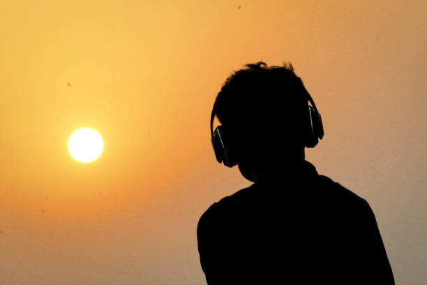 silhouette de l’homme avec un casque sur fond de ciel coucher de soleil. silhouette de musique homme heureux. - romantic sky audio photos et images de collection