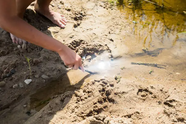 The girl is barefoot digging a groove for a stream in the sand.