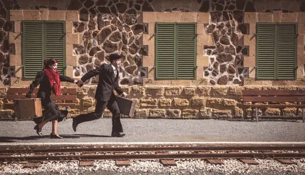 Young couple with vintage suitcase running fast outside a train station to catch the last train for journey.