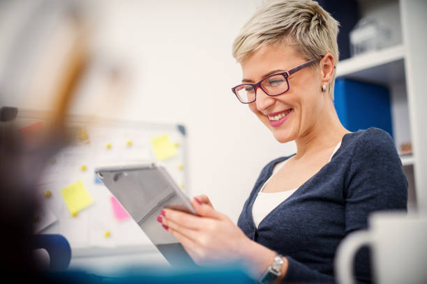 istock Young smiling secretary sitting in her office and looking at tablet. 1025402466