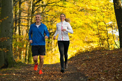 middle aged couple in their 40ies jogging through colorful indian summer autumn forrest during their workout