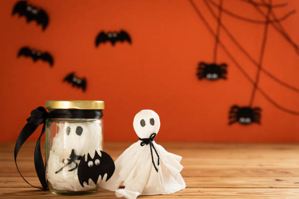 istock Halloween crafts, ghost and spide on wooden table and orange background with copy space for text. halloween concept. 1025414188