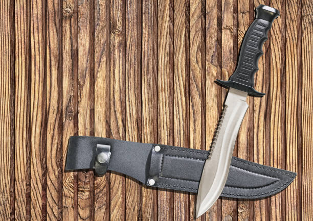 istock Fixed Blade Tactical Combat Hunting Survival Sawback Bowie Knife with Black Leather Sheath Set on Rustic Slatted Pinewood Place Mat Backdrop 1025438764