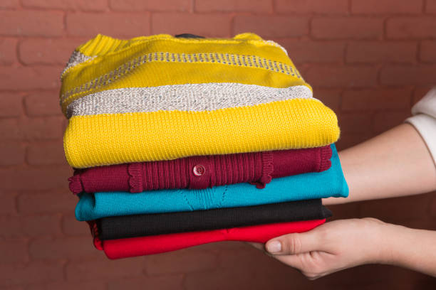 istock women's hands hold a stack of folded colored women's sweaters, against the backdrop of a terracotta brick wall, the concept of autumn and shopping 1025439130