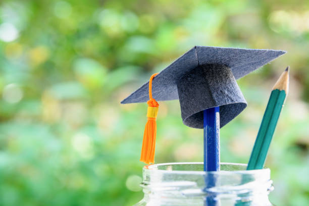 istock Education is the most powerful weapon or knowledge is power concept : Black graduation cap or hat with orange tassel on a pencil in a clear glass bottle, a green pencil with sharp tip points upward. 1025444630