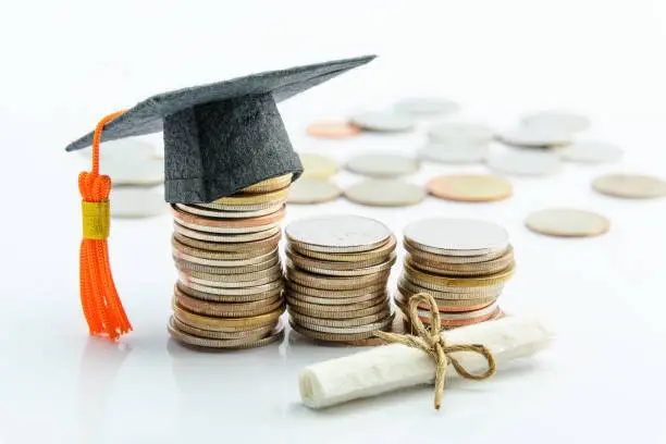 Photo of Money cost saving or money reserve for goal and success in school, higher level education concept : US dollar coins / cash, a black graduation cap or hat, a certificate / diploma on white background.