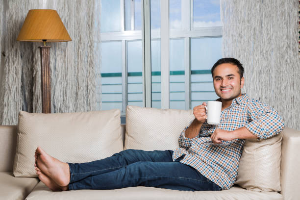 istock Attractive cheerful young man having coffee on sofa - Stock image 1025467432
