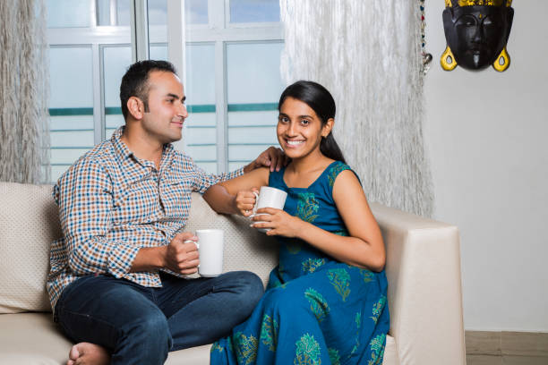 istock Cheerful young beautiful couple having coffee together on sofa - Stock image 1025473962