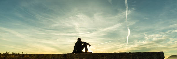 istock Man sitting on a wall watching the sunset 1025477808