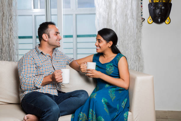 istock Cheerful young beautiful couple having coffee together on sofa - Stock image 1025477818