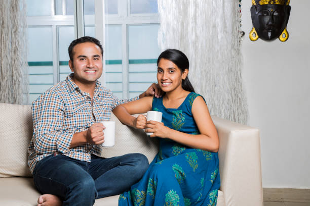 istock Cheerful young beautiful couple having coffee together on sofa - Stock image 1025480336