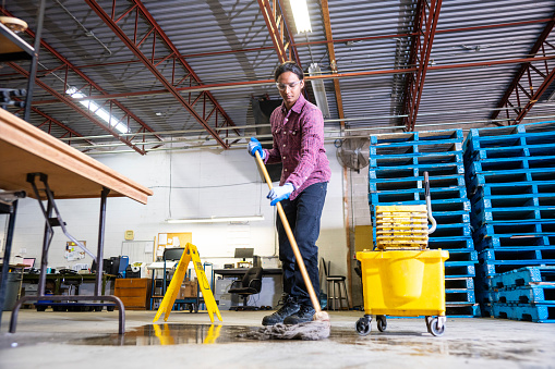 A male worker wearing work boots in a warehouse cleaning up a liquid spill on the floor.