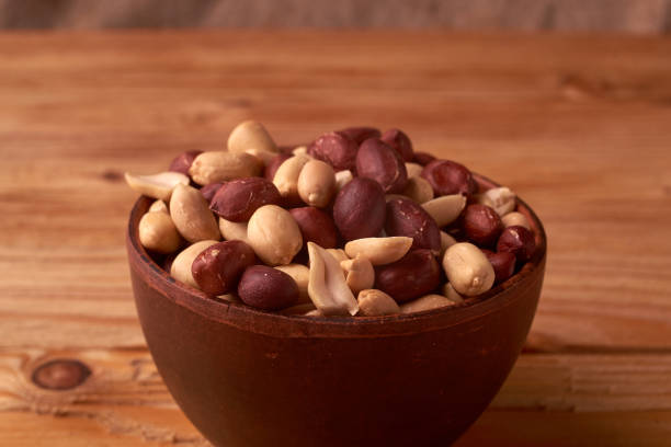 istock Deep fried peanuts in clay bowl over rustic wooden background. Selective focus 1025490598
