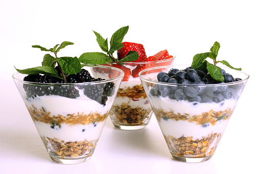 Delicious fruit, yogurt and granola cereal parfaits on white background