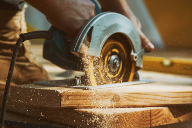 gros plan d’un menuisier à l’aide d’une scie circulaire pour couper une grande planche en bois - menuiserie photos et images de collection