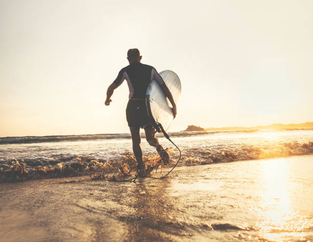 istock Surfer with surfboard runs in ocean waves, sunset time. Active lifestyle concept 1025641060