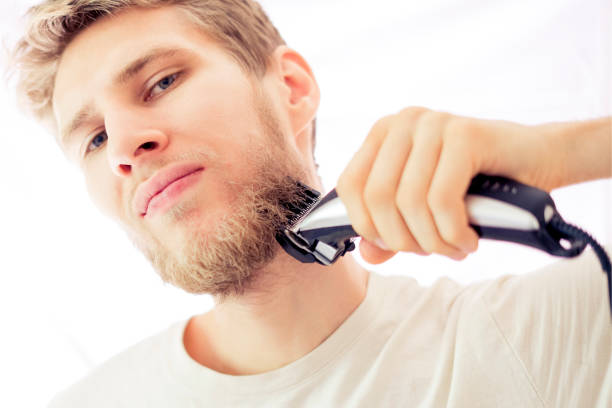 istock isolated young hipster shaving beard with machine on white background 1025666218