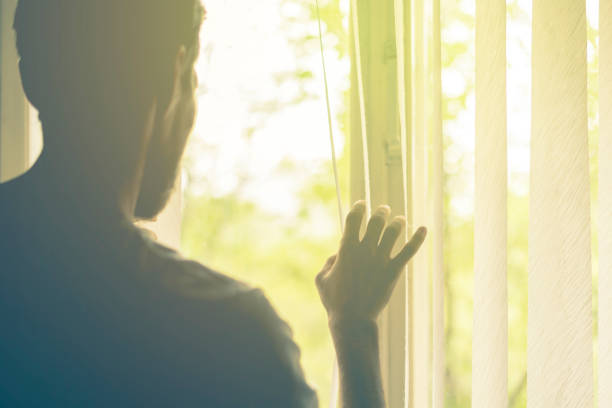istock back view of man looking through jalousie blinds on widnow at sun 1025666280