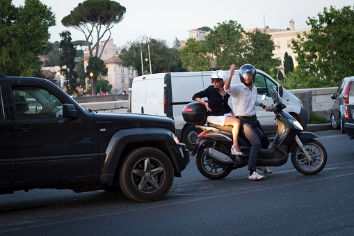 Rome, Italy: An angry biker and his passenger gesture angrily at the car that has just bumped them on a street in central Rome. Shot at dusk.