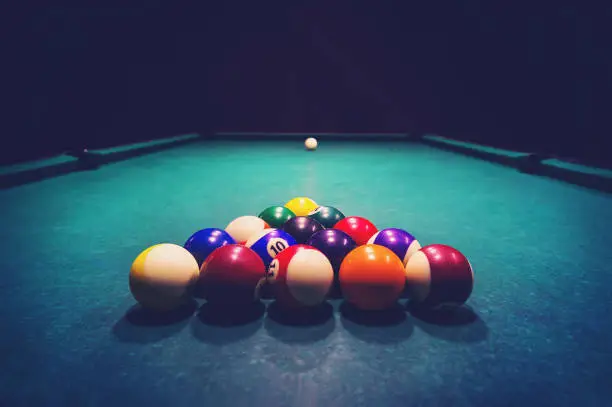 Photo of Young woman playing billiards in the dark billiard club.