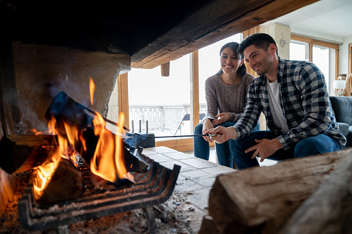 Portrait of a loving couple in a winter lodge burning logs to keep warm and looking happy - lifestyle concepts