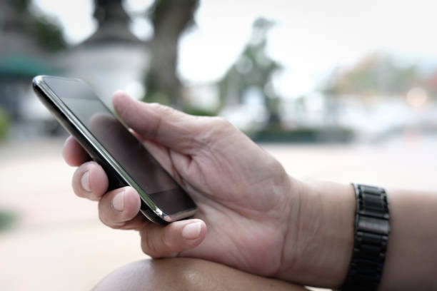 istock man holding mobile phone. hand texting message, using app with smartphone outdoor 1025815372
