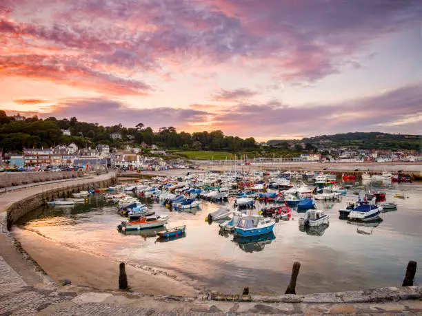The historic harbour at Lyme Regis, Dorset, England, on a summer evening, with the Cobb and boats under a red sunset sky.
