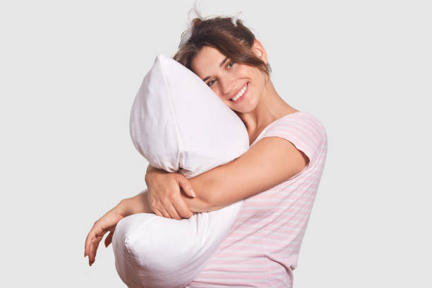 istock Glad optimistic female has toothy smile, shows white perfect teeth, leans on pillow, has appealing look, being in high spirit after pleasant dreams, isolated over white background. Healthy lifestyle 1025834758