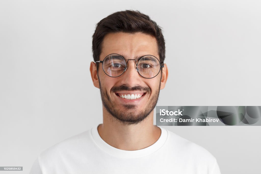 白い t シャツと丸い眼鏡、カメラを見て、積極的に笑顔を着て、灰色の背景に分離された若いハンサムな白人男性の昼間の肖像画 - 男性のロイヤリティフリーストックフォト