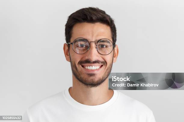 Daylight Portrait Of Young Handsome Caucasian Man Isolated On Grey Background Dressed In White Tshirt And Round Eyeglasses Looking At Camera And Smiling Positively Stock Photo - Download Image Now