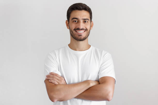 Portrait of smiling handsome man in white t-shirt, standing with crossed arms isolated on gray background Portrait of smiling handsome man in white t-shirt, standing with crossed arms isolated on gray background italian ethnicity stock pictures, royalty-free photos & images
