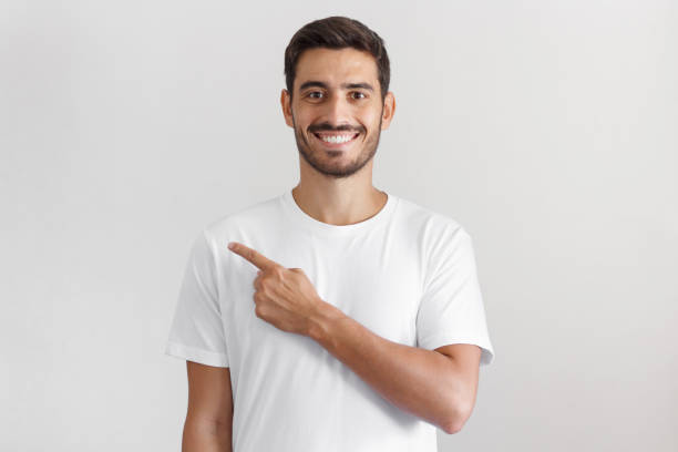 istock Handsome man in white t-shirt pointing left with finger isolated on gray background 1025855504