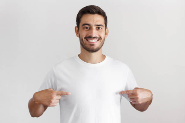 istock Smiling nice man pointing at blank white t-shirt with both index fingers, copy space for your advertising, isolated on grey background 1025855514