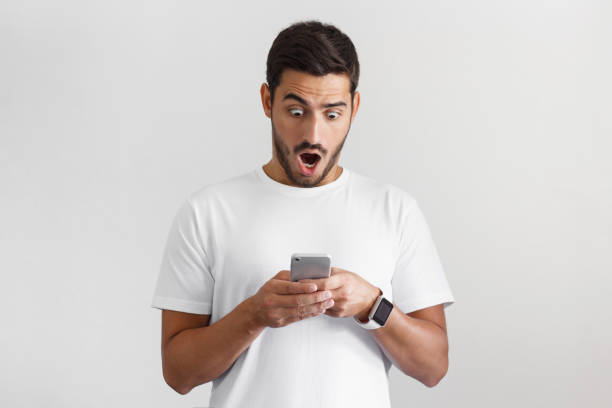 istock Portrait of young man isolated on gray background, impressed by media content from web on display of her smartphone 1025855536