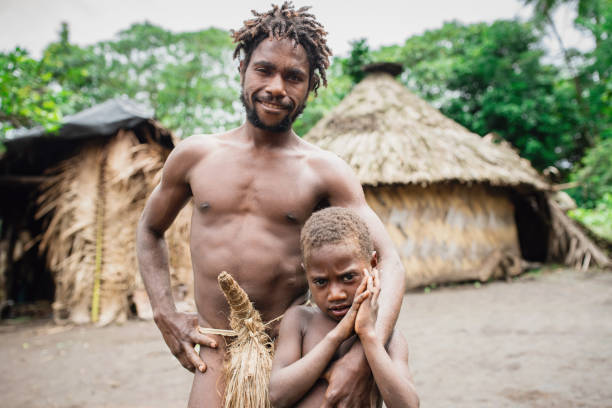 Tanna Island Tribal Chief and Son Kastom Village Vanuatu Tanna Island, Vanuatu - December 3rd, 2017: Happy Smiling Melanesian Tribal Chief wearing tribal penis sheaths together with his young son in front of their Village Hut in remote Tribal Kastom Village. Tafea Province, Tanna Island, Vanuatu, Oceania. koteka stock pictures, royalty-free photos & images