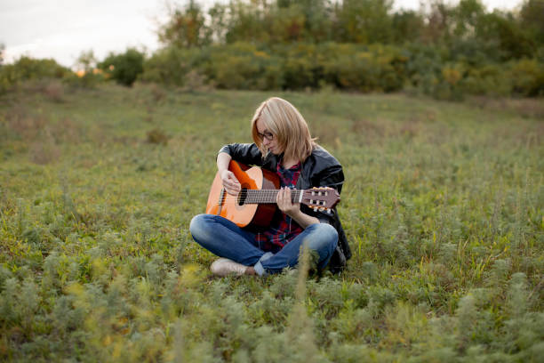 istock girl sits on the grass with a guitar playing, putting her hands on the strings 1025882814