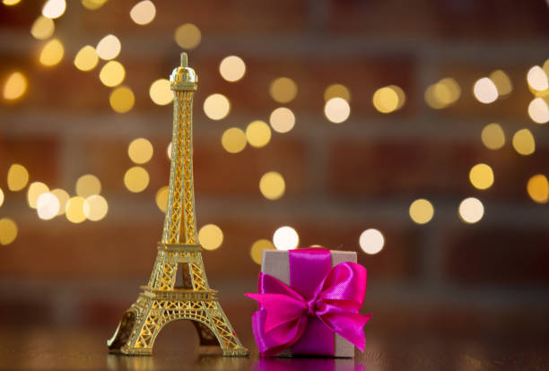 handmade gift box with purple bow and Eiffel tower golden souvenir on wooden table with fairy lights on bokeh background