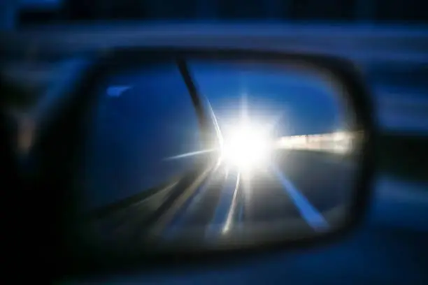 Star reflection of cars long lights in rear view mirror at sunset.