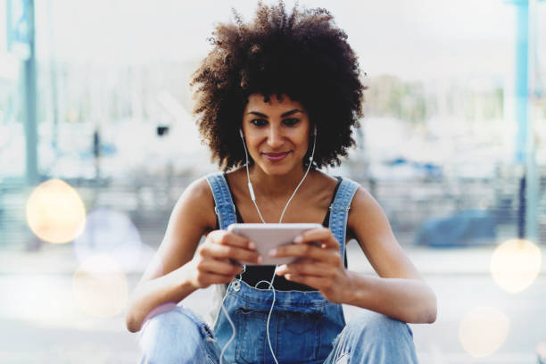 istock charming dark-skinned girl with afro hair watching video on mobile phone using public network wifi outside. Modern female entrepreneur communicates via video link with her personal assistant 1025941692