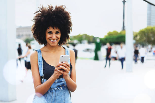 istock a beautiful dark-skinned smiley girl communicates in a group chat with friends through the application on the smartphone outside. Female traveler is guided in the city on the e-map in her cellphone. 1025941702