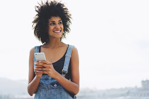 Portrait of beautiful mixed race woman chatting online via smartphone sending messages spending time outside,pretty hipster girl using application on mobile phone for online banking using public wifi
