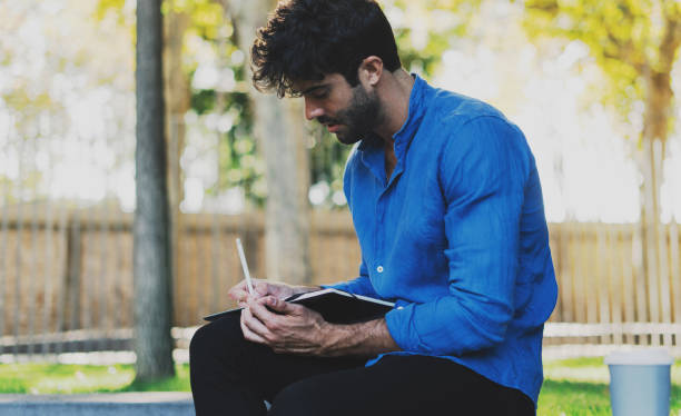 istock Public relations specialist working on a new press release for the new product while drinking coffee outside the office. Hipster guy writing ideas while planning the journey to the mountains. 1025944986