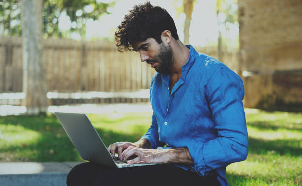 istock Marketing specialist preparing presentation of new project by using portable computer outside the office. Bearded man typing message on a laptop sitting outdoors. 1025945148