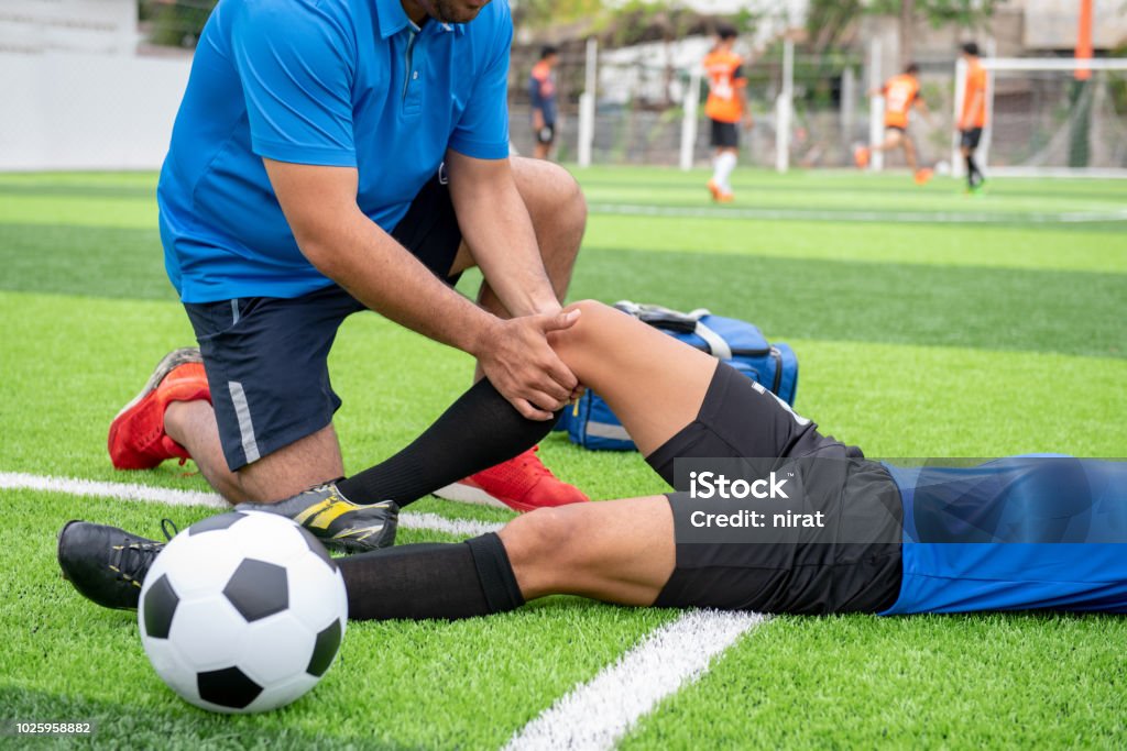 Futbolista con una camisa azul, pantalón negro, lesionados en el césped durante la carrera. - Foto de stock de Lesión física libre de derechos