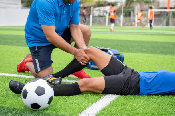 futbolista con una camisa azul, pantalón negro, lesionados en el césped durante la carrera. - lesión física fotos fotografías e imágenes de stock
