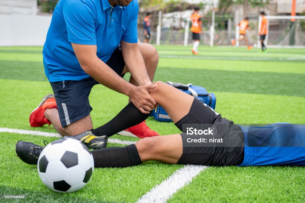 Footballeur, vêtu d’une chemise bleue, pantalon noir, blessé dans la pelouse pendant la course. - Photo de Blessure physique libre de droits