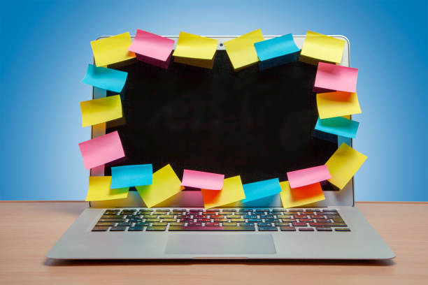 istock Laptop in reminders with colored stickers notes on the display frame on table with blue wall. Many unfulfilled tasks 1025959606