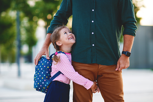 first day at school. father leads a little child school girl in first grade