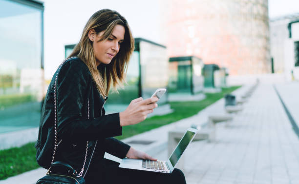 istock Freelancer female planning her weekend journey by searching information online using a mobile phone and a portable computer connected to wifi while enjoying time in a city park on a sunny day 1025966996